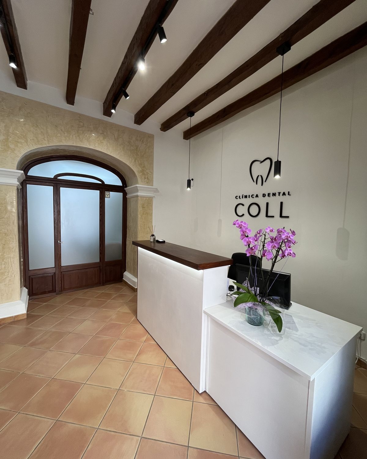 Recepción de Clínica Dental Coll, con vigas de madera y arco de piedra, en Santa Maria del Camí